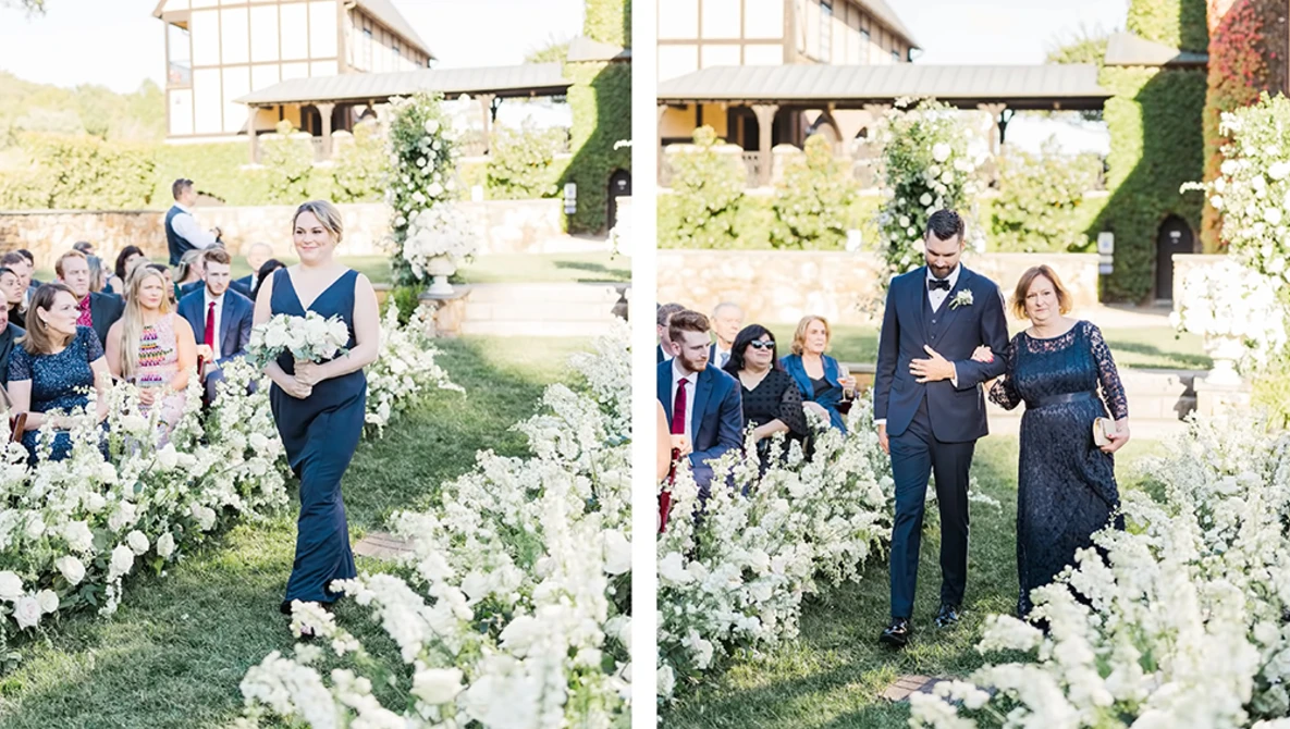 Wedding ceremony with guests walking through white flowering plants lining an outdoor garden aisle.