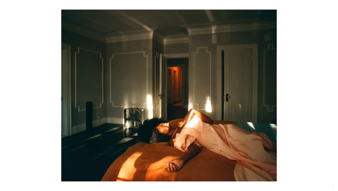 Sunlit bedroom with unmade bed featuring orange bedding and white walls with paneling.