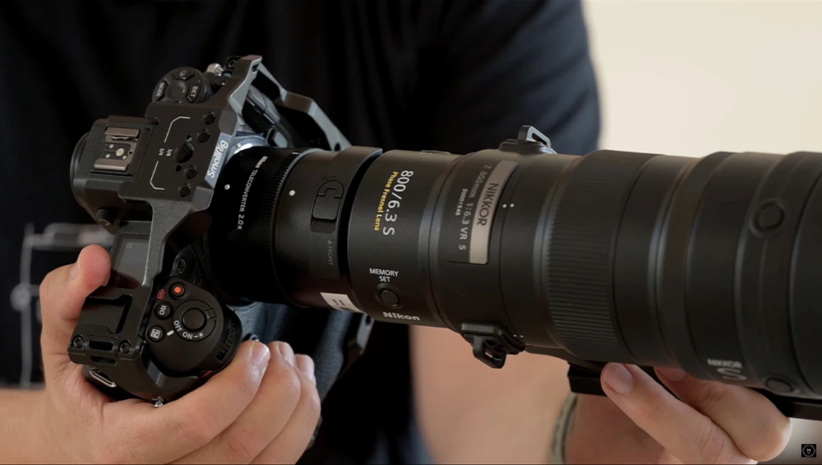 Photographer's hands holding a mirrorless camera with a telephoto lens attached.