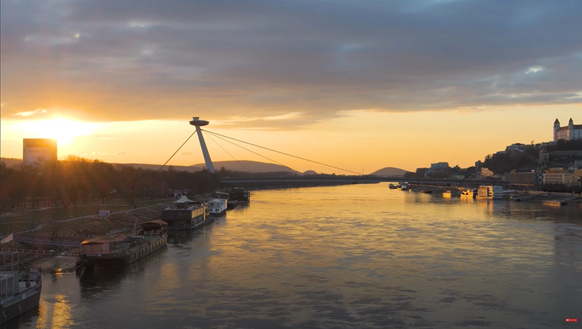 Cable-stayed bridge spanning a river at golden hour sunset with warm reflections on water.
