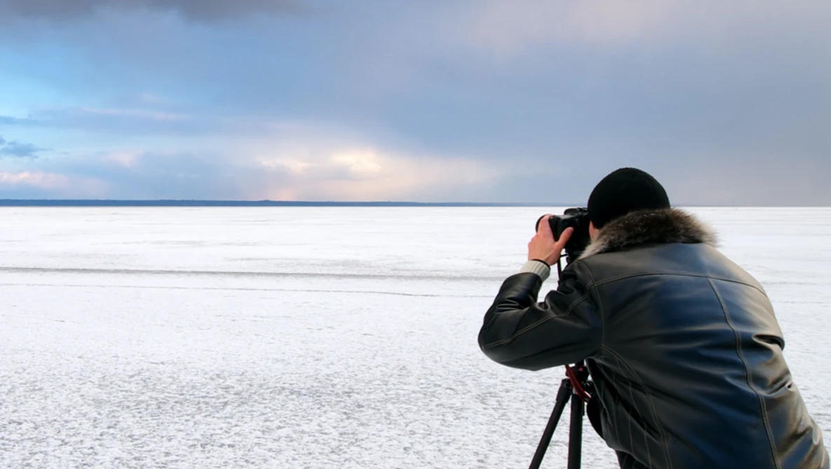 Photographer with tripod-mounted camera capturing a frozen landscape at twilight.