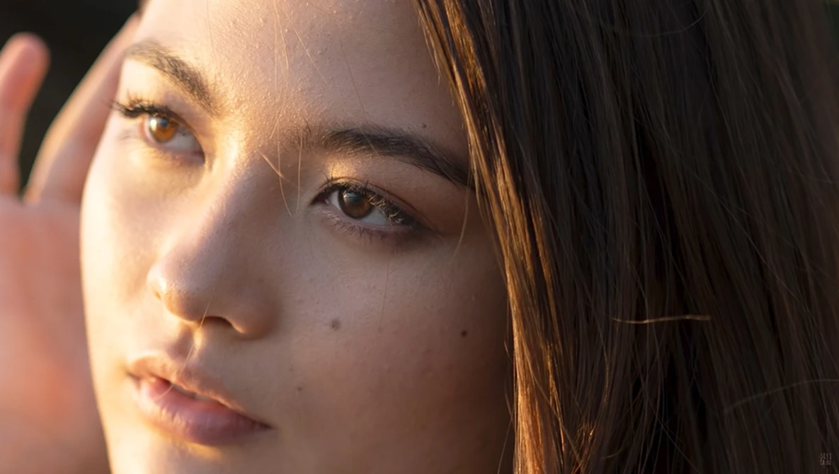 Woman's face in golden hour sunlight, looking directly at camera with natural expression.