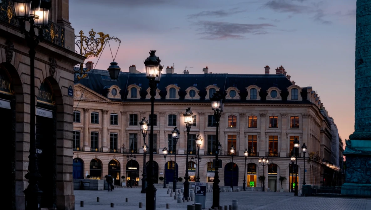 Ornate Parisian building facade illuminated at dusk with street lamps and mansard roof.