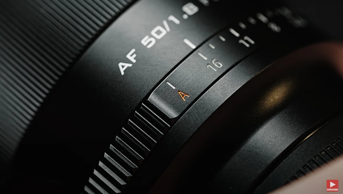 Close-up of camera lens barrel showing AF autofocus markings and distance scale in dramatic side lighting.