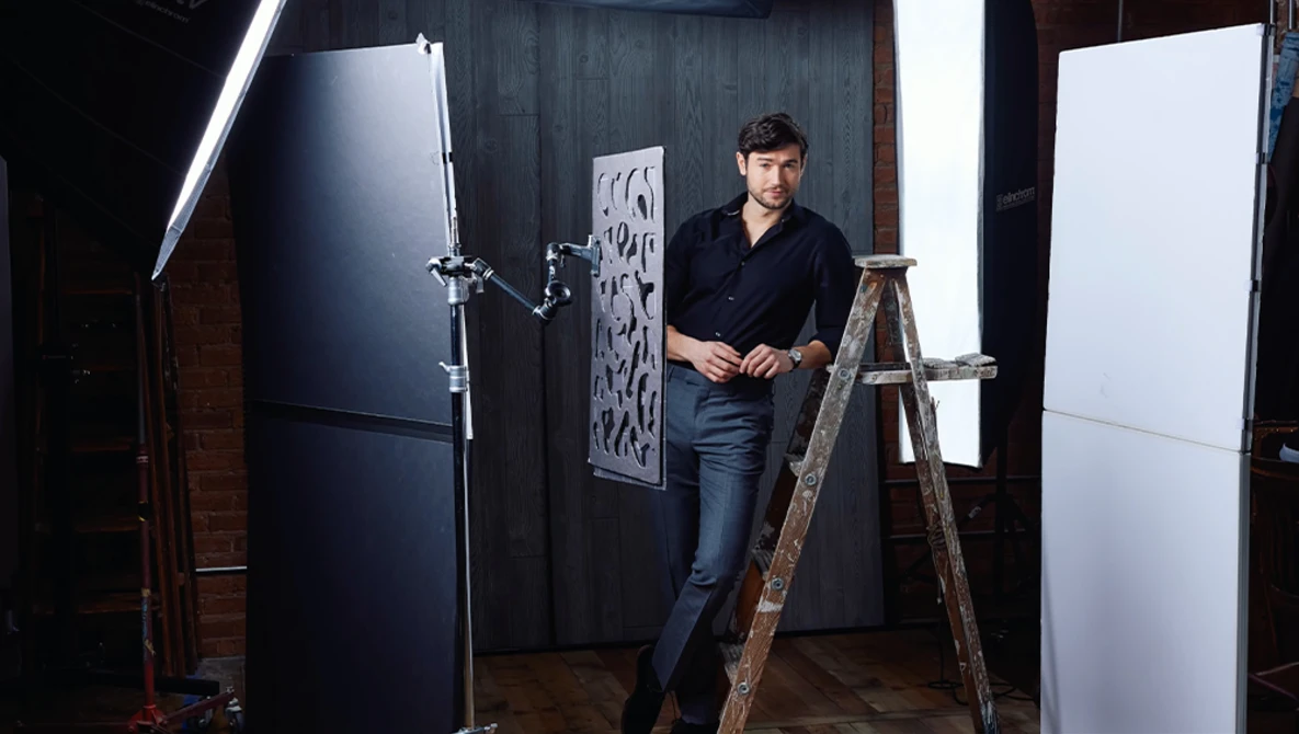 Photographer standing on a wooden ladder in a studio setup with professional lighting equipment and reflectors.