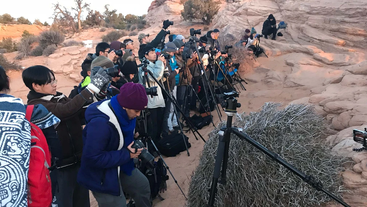 Large group of photographers with telephoto lenses and tripods positioned on a rocky outcrop.