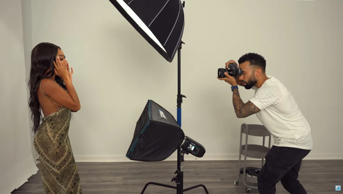 Photographer shooting a portrait subject in a studio with professional lighting setup.