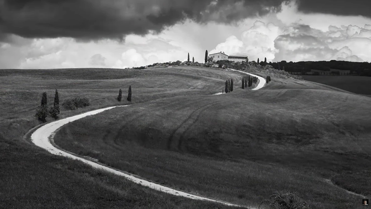 Winding white road cutting through rolling hills in black and white landscape photography.