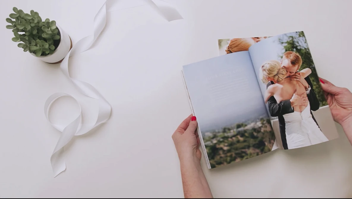 Hand holding open wedding photo album with couple image visible on pages.