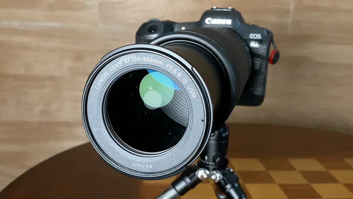 Canon EOS camera with telephoto lens mounted on tripod, showing rear lens elements and green lens cap.