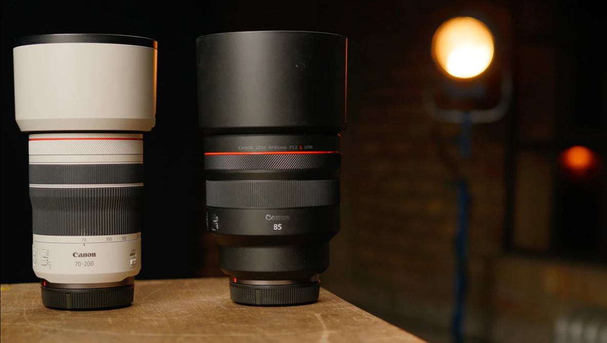 Two telephoto lenses side by side on wooden surface with warm studio lighting in background.