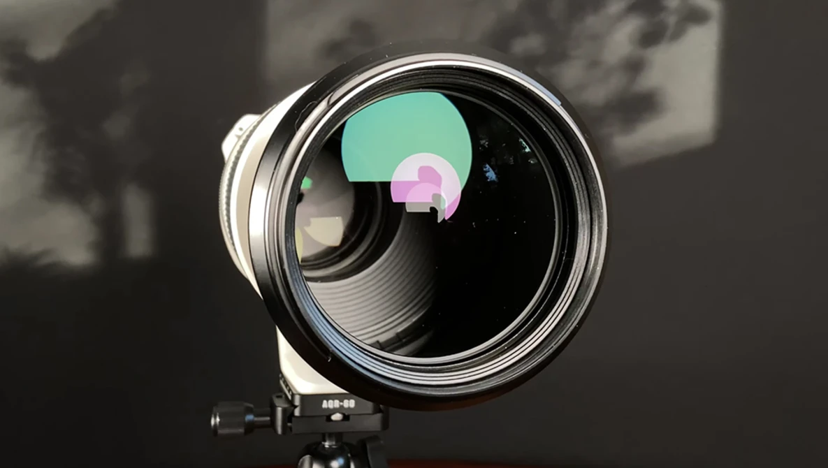Large telephoto lens mounted on a tripod with colorful lens element visualization overlaid on the front glass.