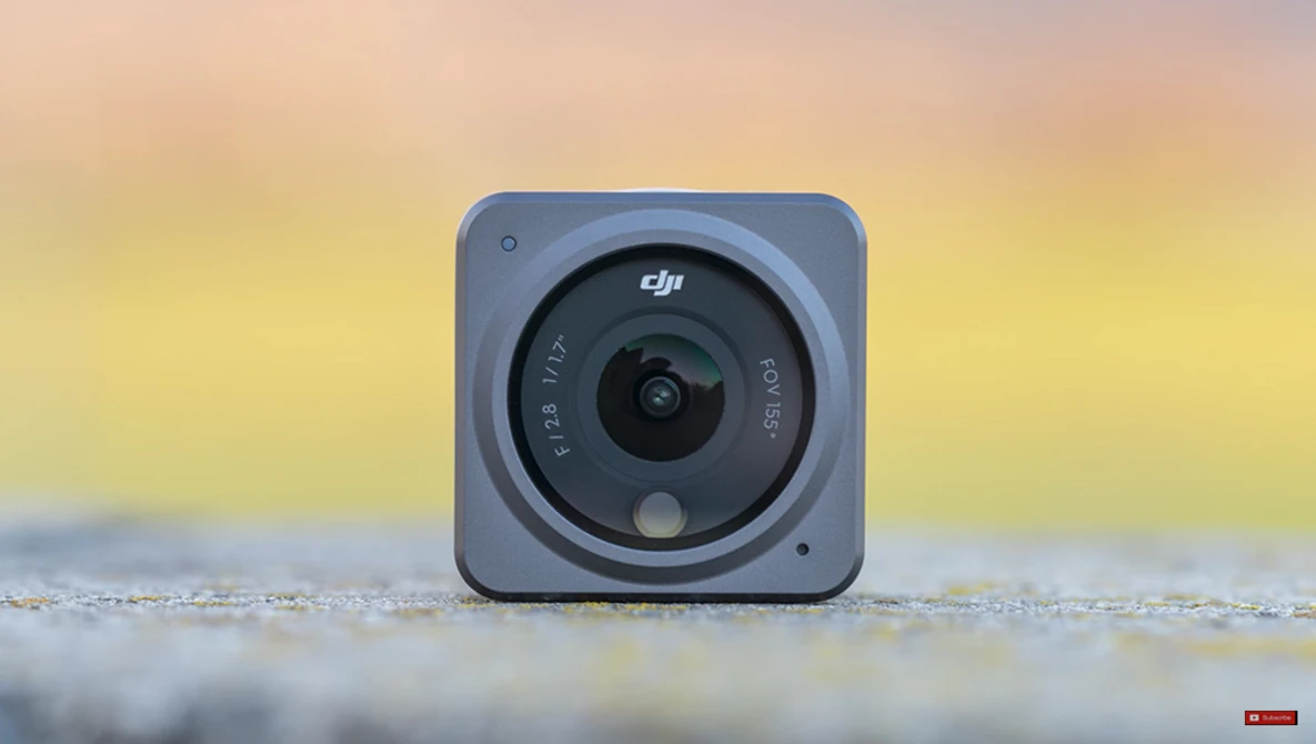 DJI action camera with square body and circular lens mounted on wet surface with blurred golden sunset background.