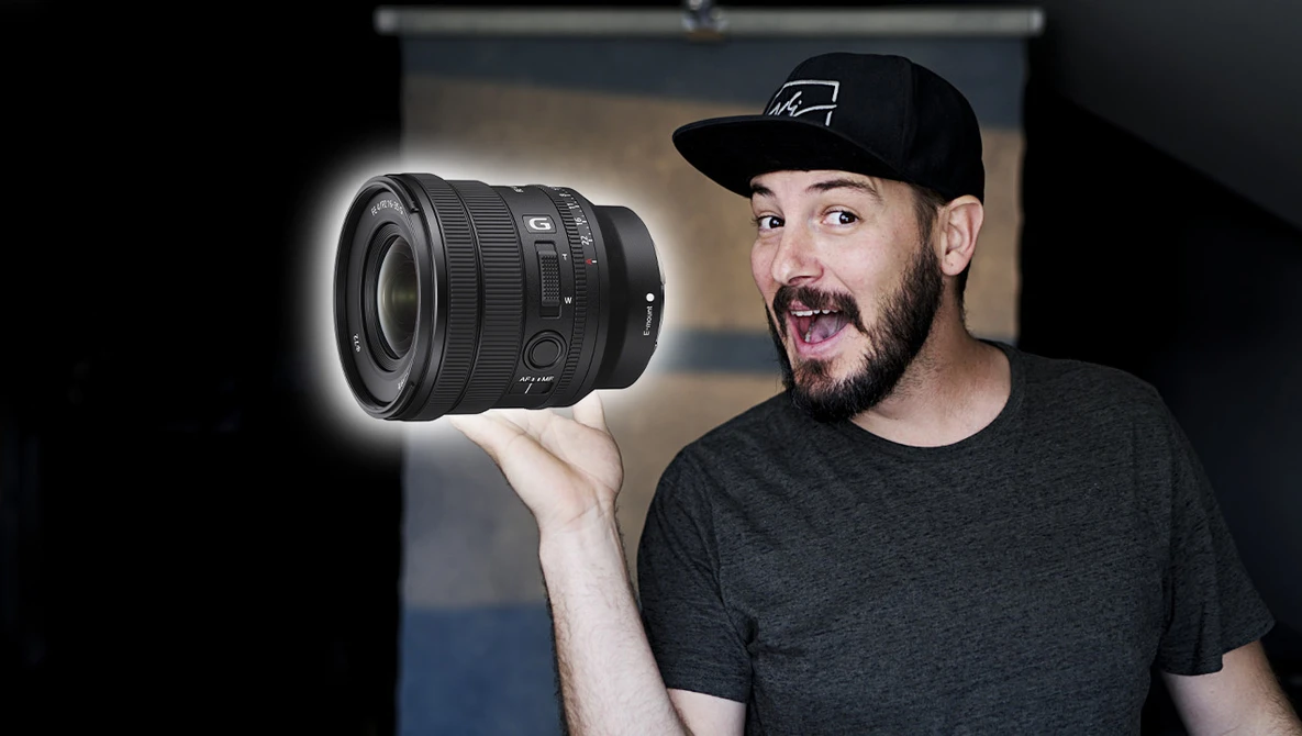 Photographer holding a Sony lens with surprised expression against blurred studio background.
