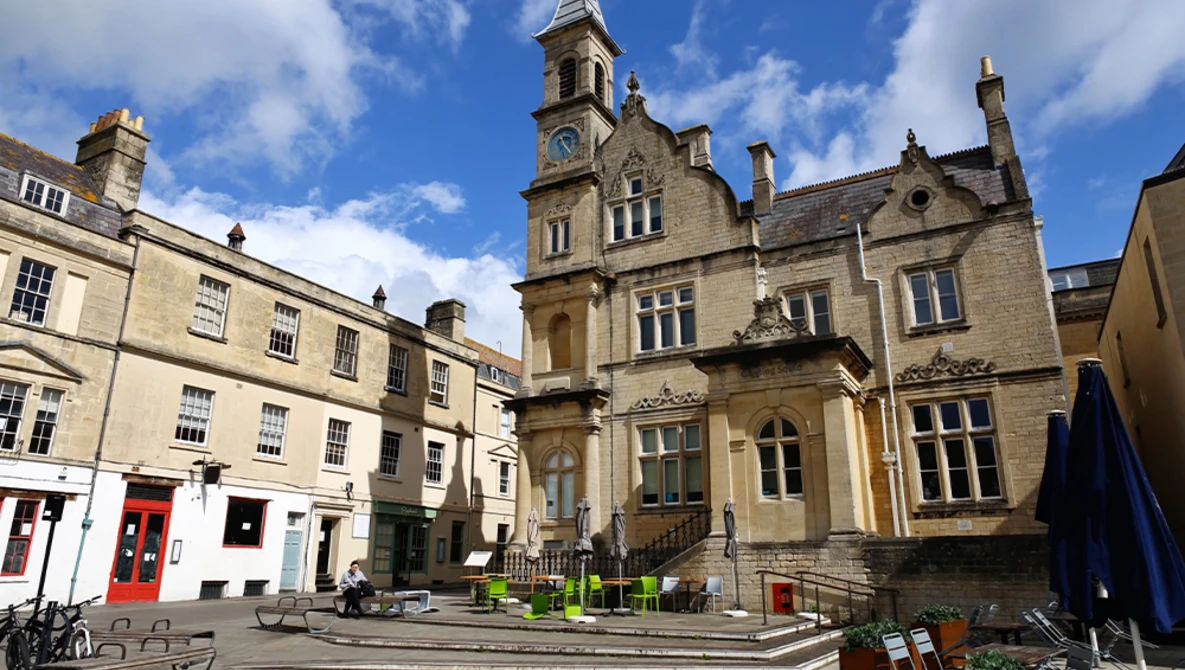 Stone Victorian building with clock tower overlooking a courtyard with contemporary seating areas.