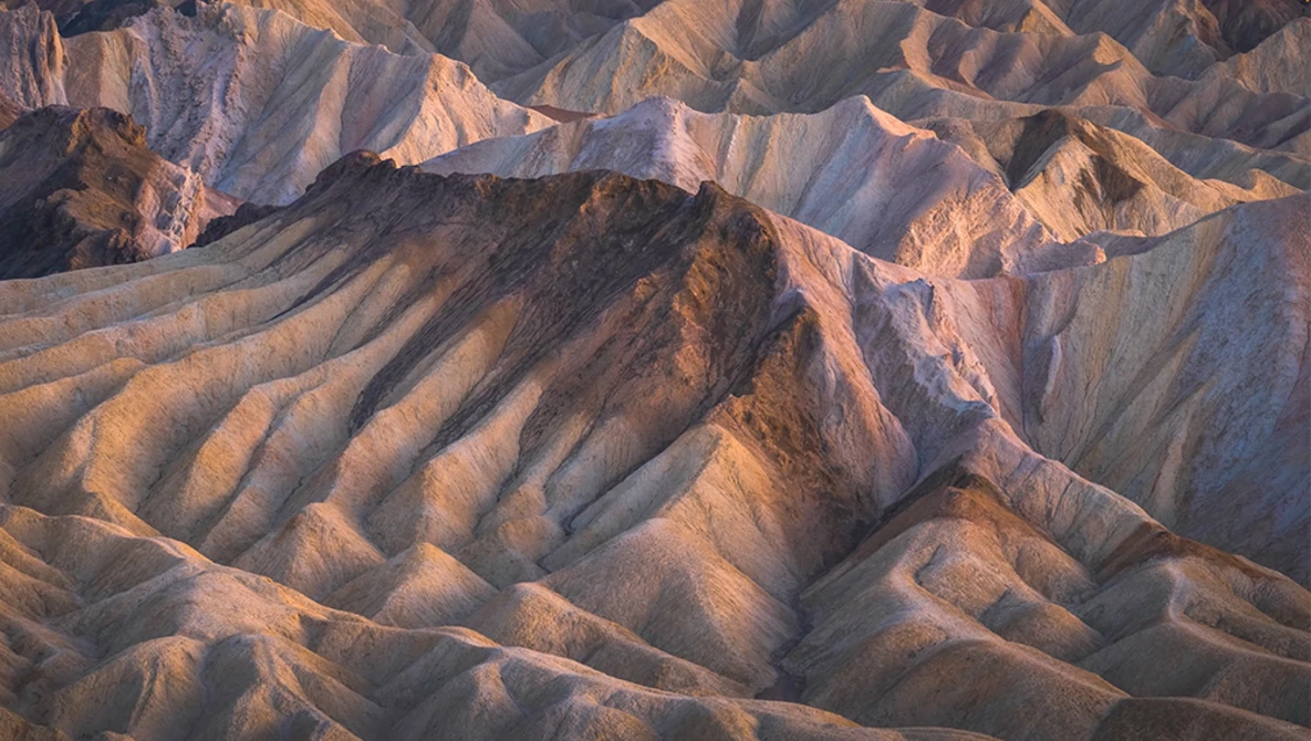 Layered badlands landscape with deeply eroded ridges and ravines bathed in golden hour sunlight.