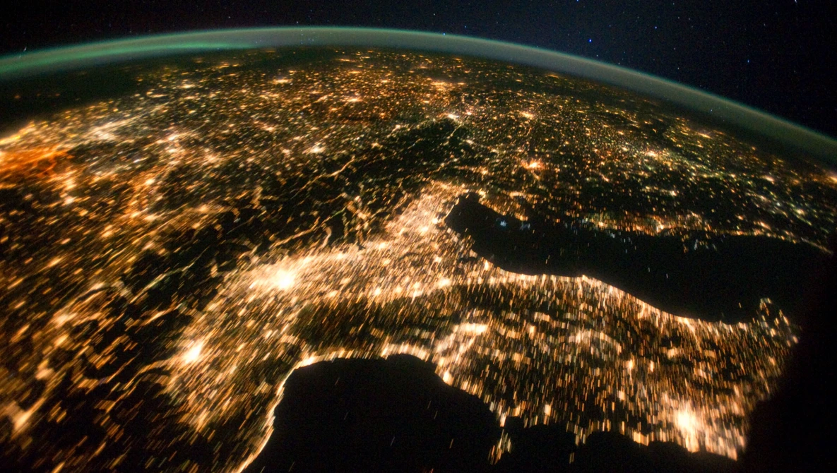 Earth at night photographed from space, showing city lights scattered across continents against a dark starry sky.