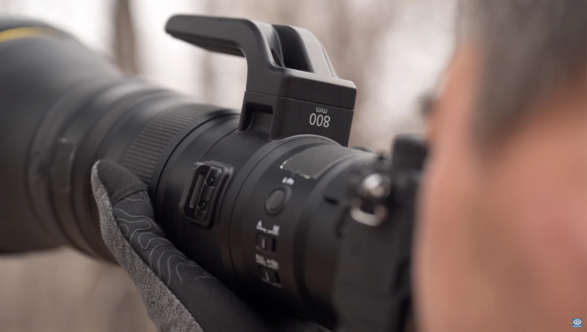 Close-up of a telephoto lens mounted on a camera with a pop-up flash positioned above the lens barrel.