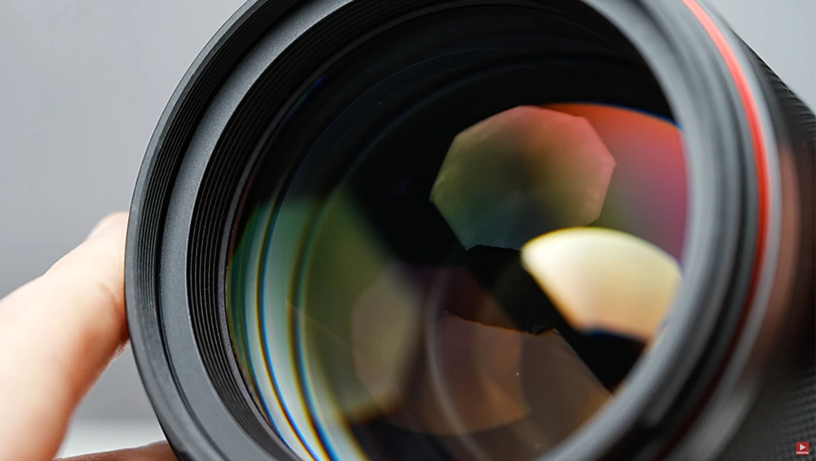 Close-up view of a camera lens barrel showing colorful optical glass elements and coatings.