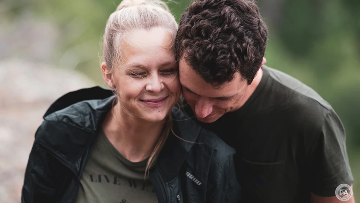 Two people embracing outdoors with blurred green foliage background.