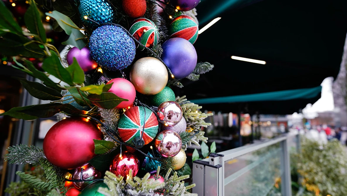 Colorful Christmas ornaments and garland arranged on an outdoor railing at night.