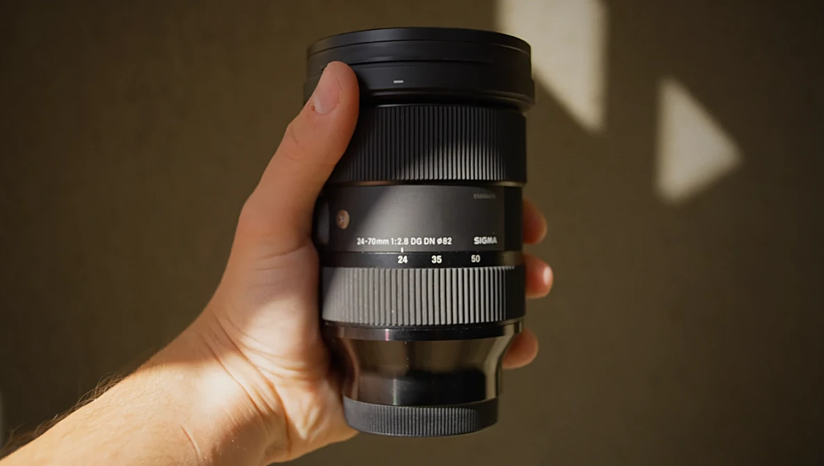 Hand holding a telephoto zoom lens with white and black barrel against a neutral background.