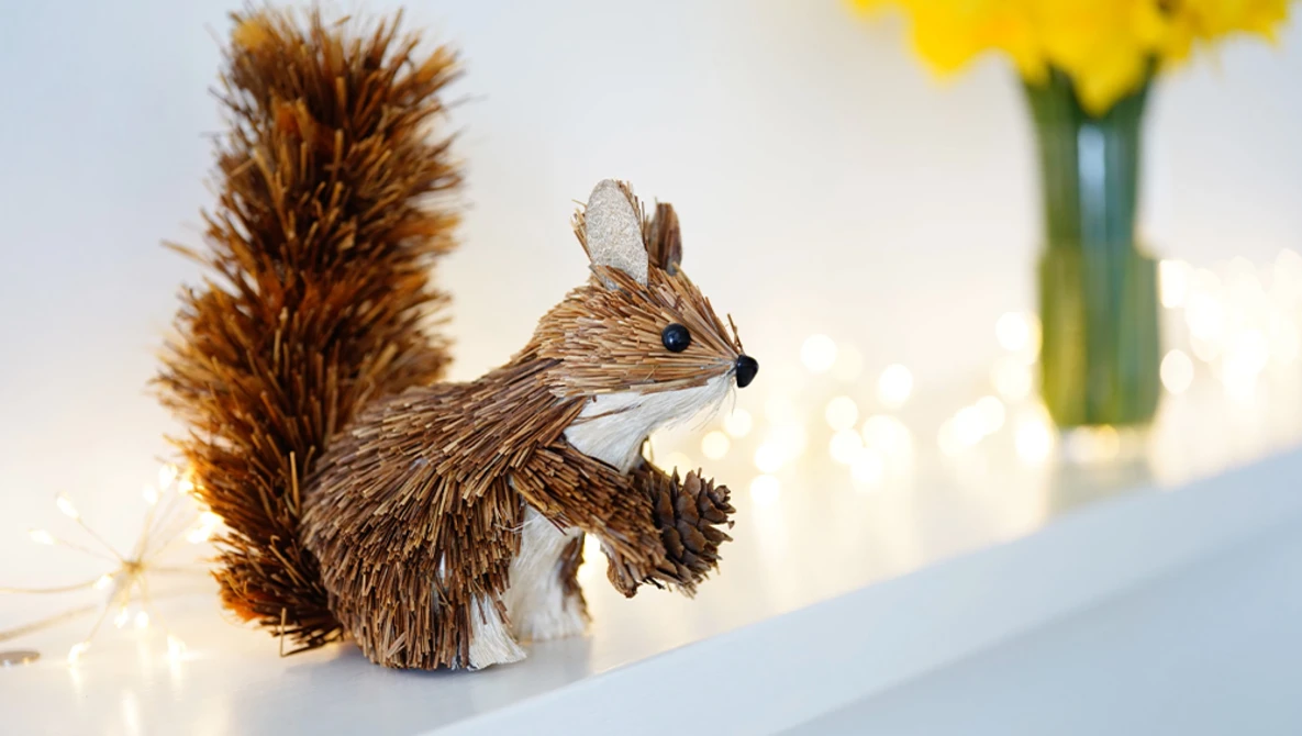 Decorative squirrel figurine crafted from twine or raffia material, photographed against a soft, bokeh background.