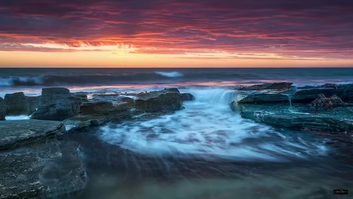 Coastal seascape at sunrise with silky water flowing around dark rocky outcrops.