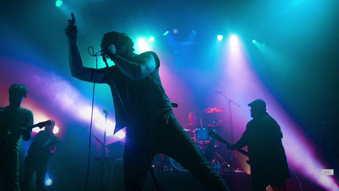 Lead singer performing center stage with microphone stand, bathed in vibrant blue and purple concert lighting.
