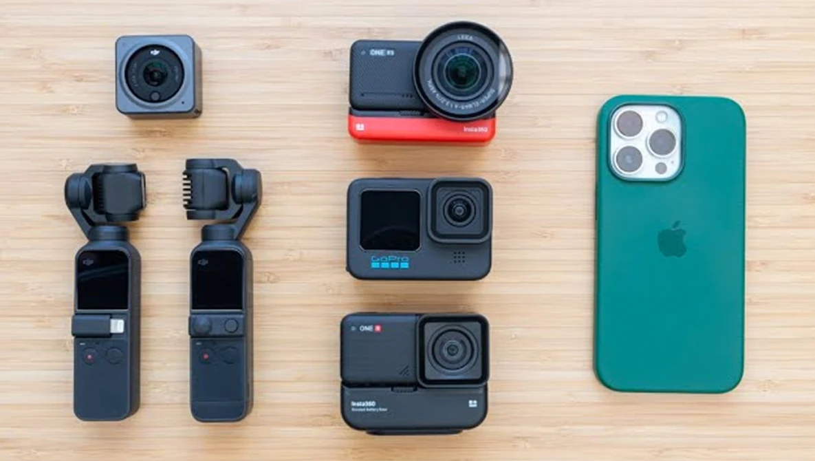 Collection of compact cameras and smartphone arranged on light wood surface.
