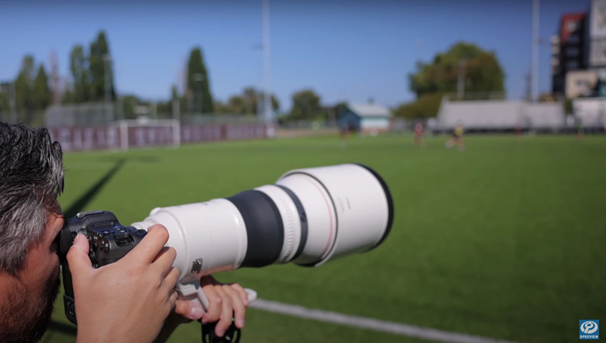 Photographer with telephoto lens photographing a soccer field during daytime.
