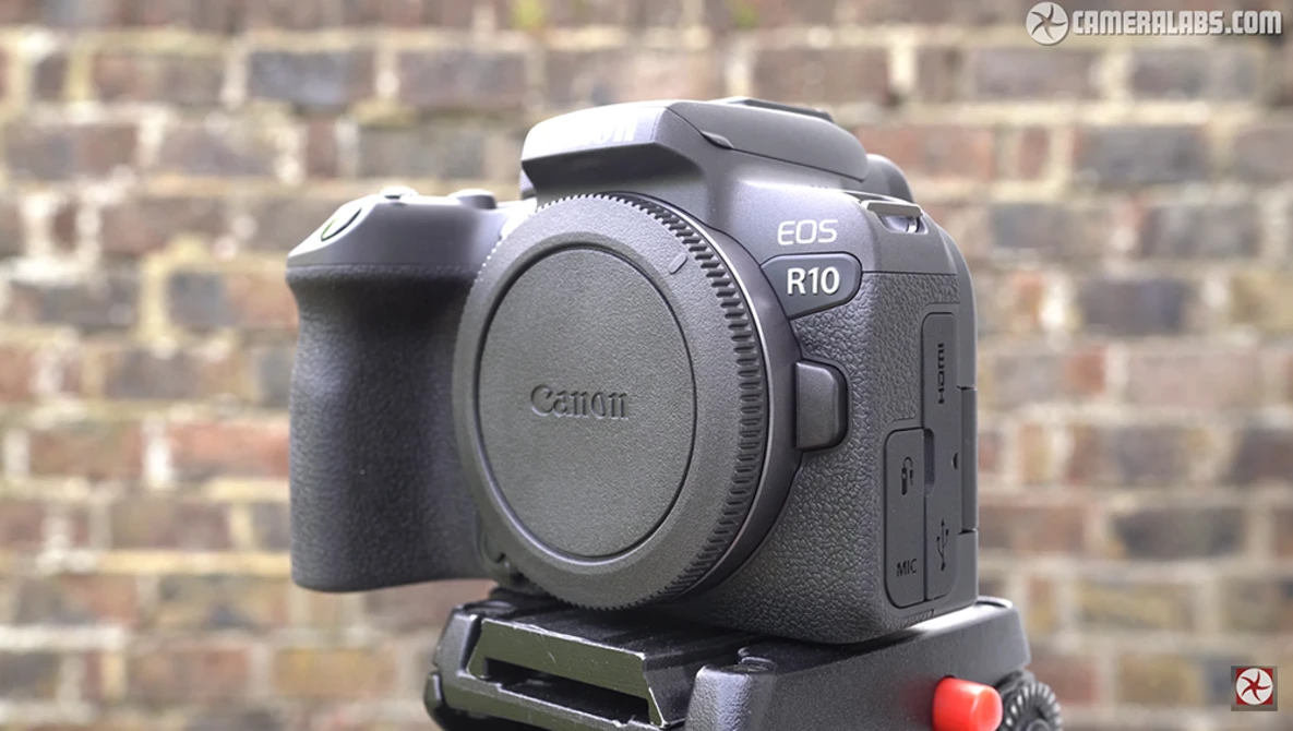 Canon EOS R10 mirrorless camera body mounted on a tripod head against a brick wall.