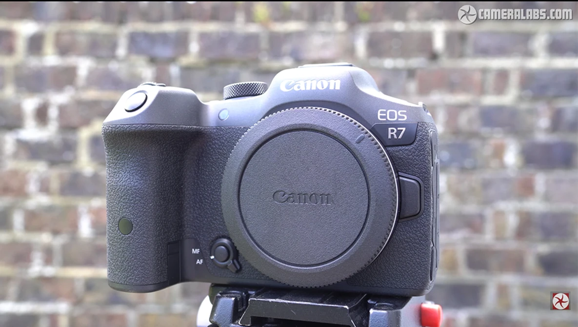 Canon EOS R7 mirrorless camera body mounted on a tripod against a brick wall background.
