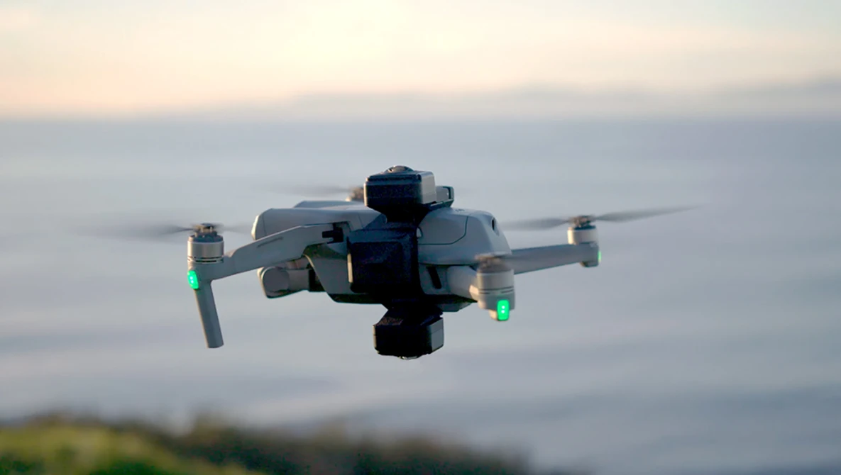 DJI Mavic drone with propellers spinning against a blurred coastal landscape at sunset.