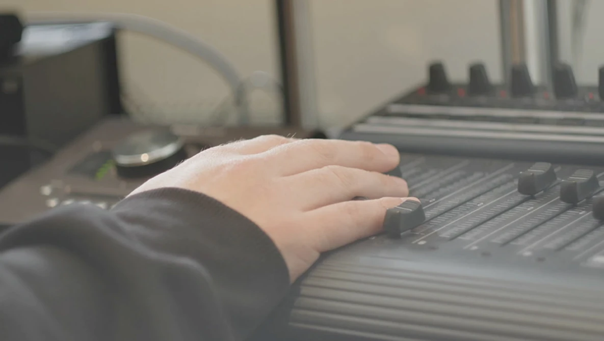 Child's hand resting on a keyboard in a home office setting with blurred computer equipment in the background.