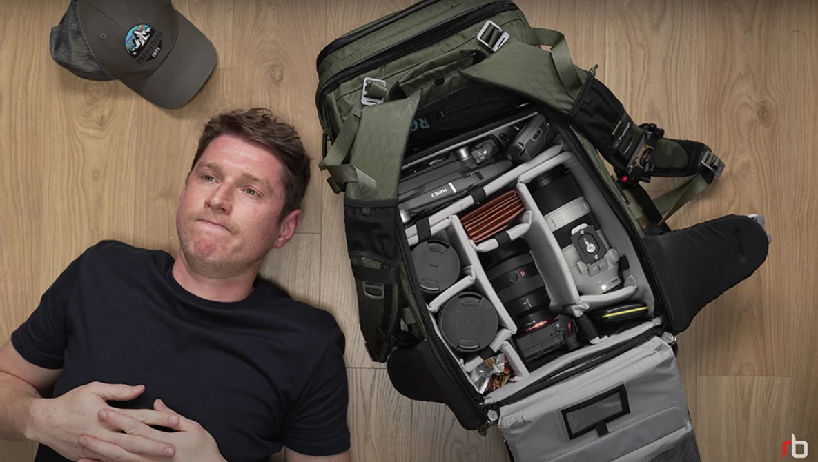 Photographer lying beside an open camera backpack displaying organized photography gear and equipment.