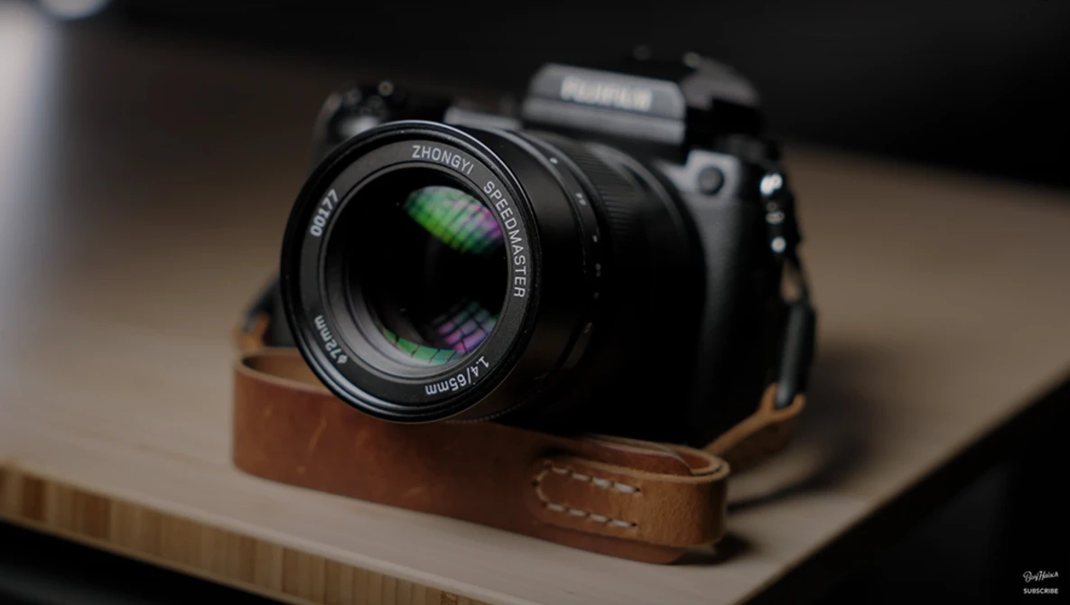 Mirrorless camera with prime lens mounted on brown leather half-case, positioned on wooden surface.