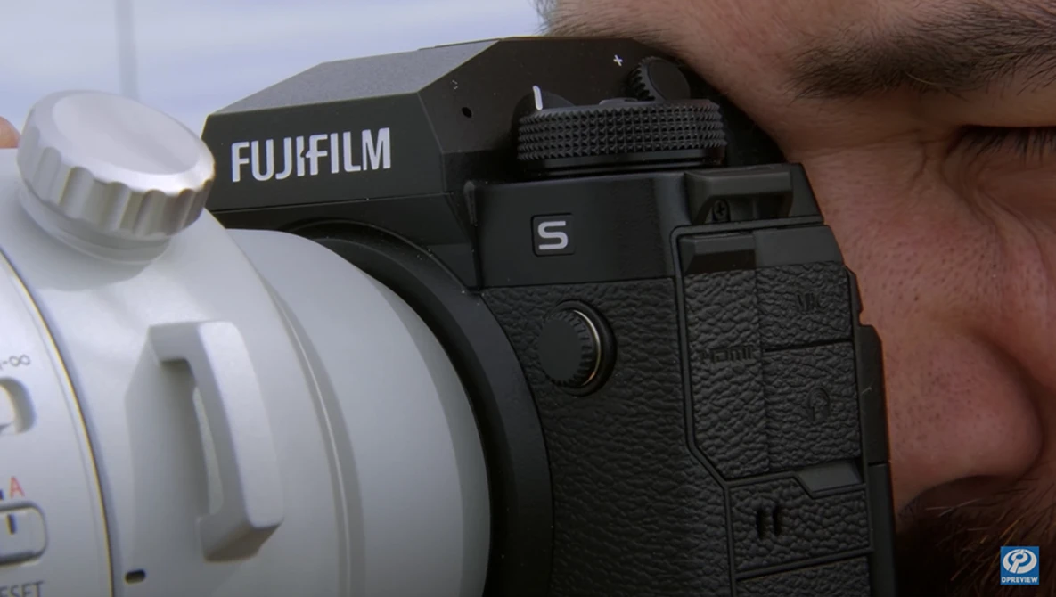 Photographer holding a Fujifilm S camera with white telephoto lens mounted.