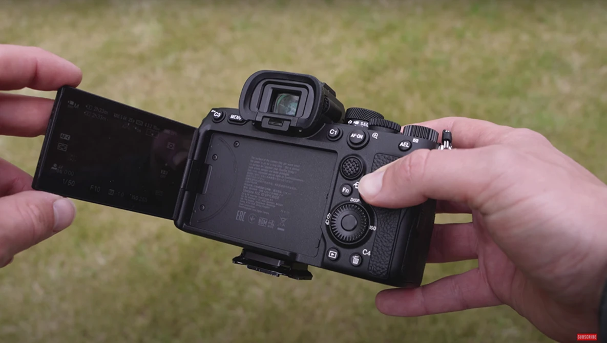 Hands holding a mirrorless camera with articulating LCD screen flipped out to the side.