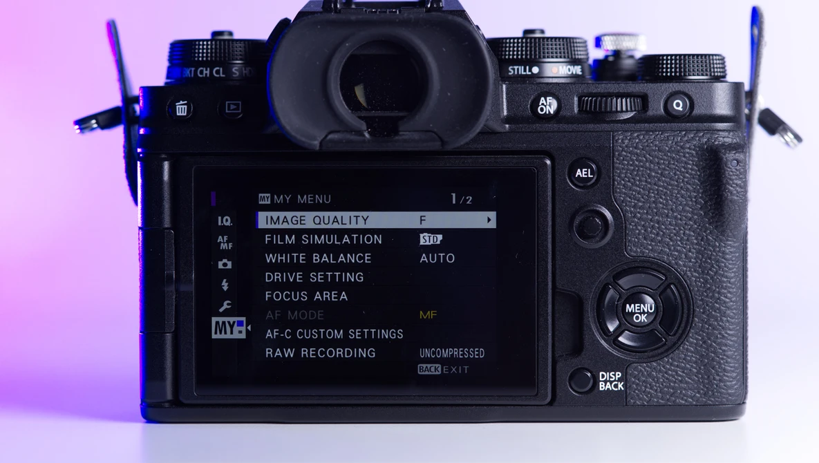 Mirrorless camera displayed from above with rear LCD screen showing menu settings against pink and purple gradient lighting.