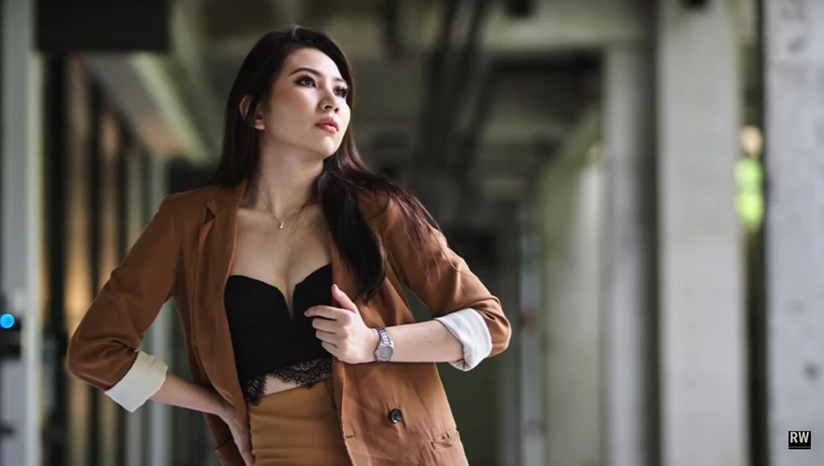 Woman in brown blazer and black top standing in modern corridor, looking upward with contemplative expression.