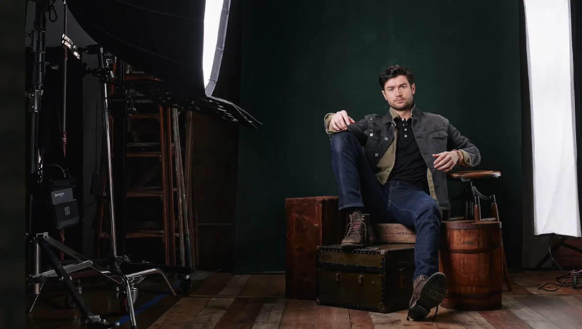 Man seated on wooden crates in studio setting with professional lighting setup.