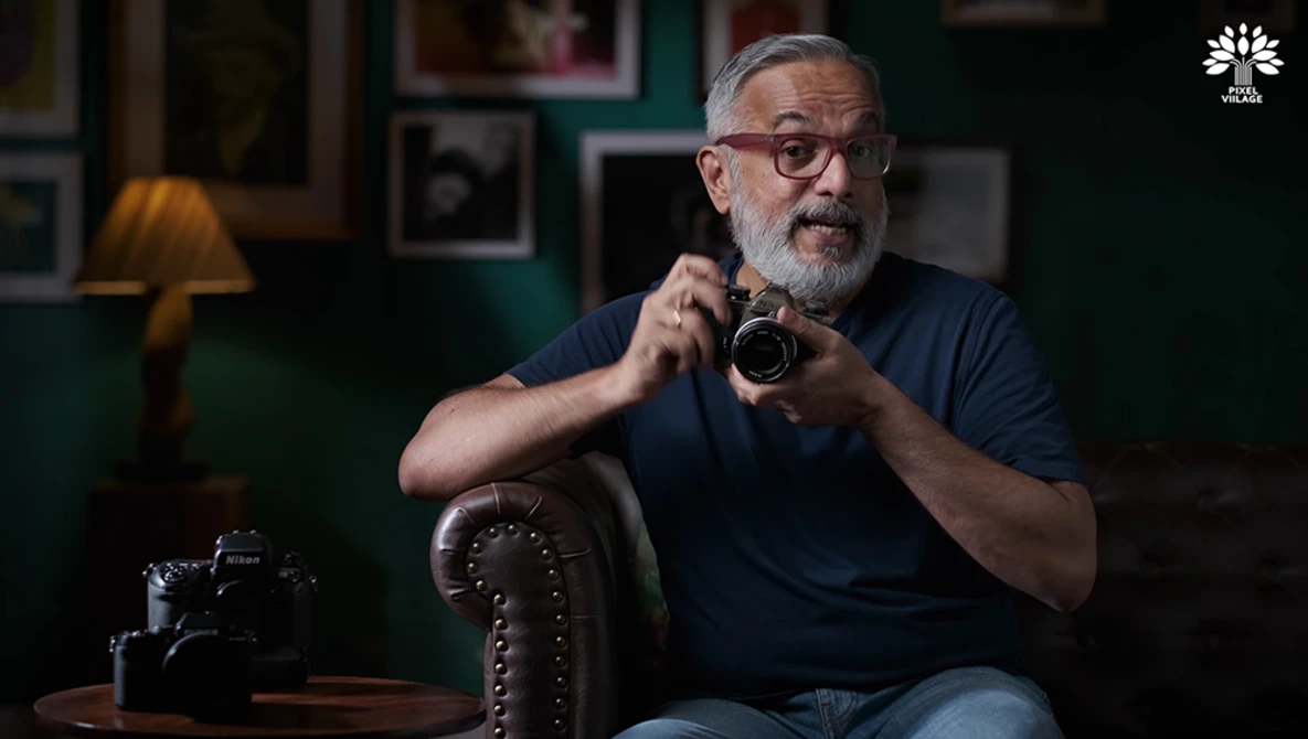 Bearded man with glasses holding a vintage camera while seated in a studio setting.