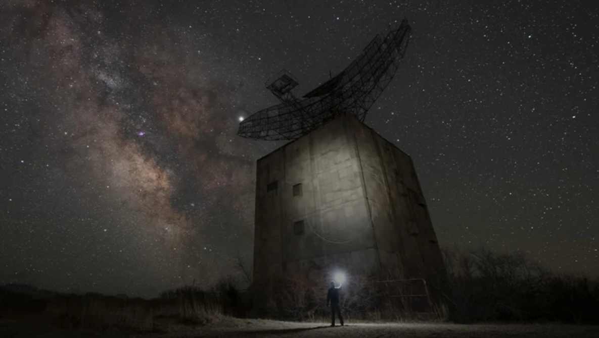 Silhouetted figure standing before an abandoned windmill beneath the Milky Way.