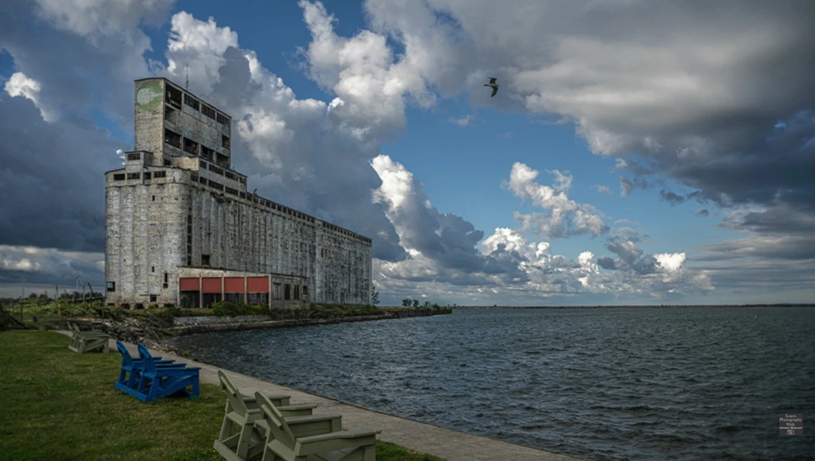 Abandoned concrete grain elevator beside Lake Michigan with dramatic cumulus clouds.