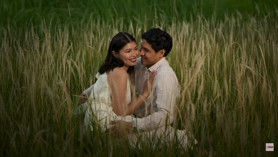 Couple embracing in a tall grain field during golden hour with soft, warm lighting.