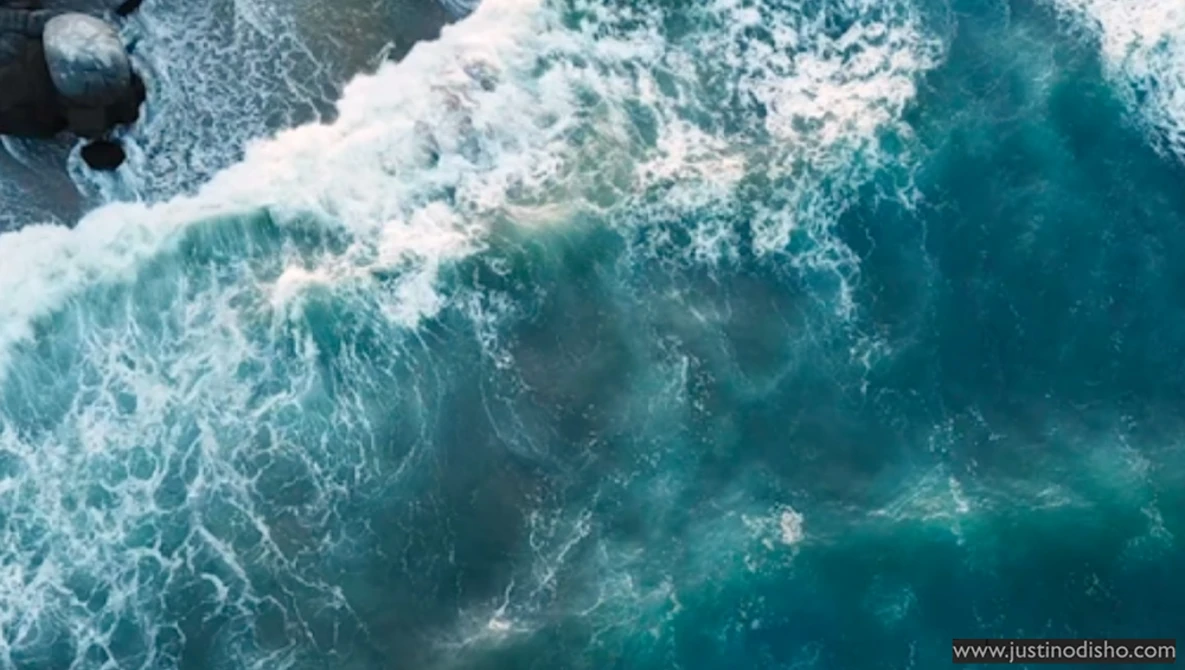 Aerial view of ocean waves crashing on a beach with white foam and turquoise water.