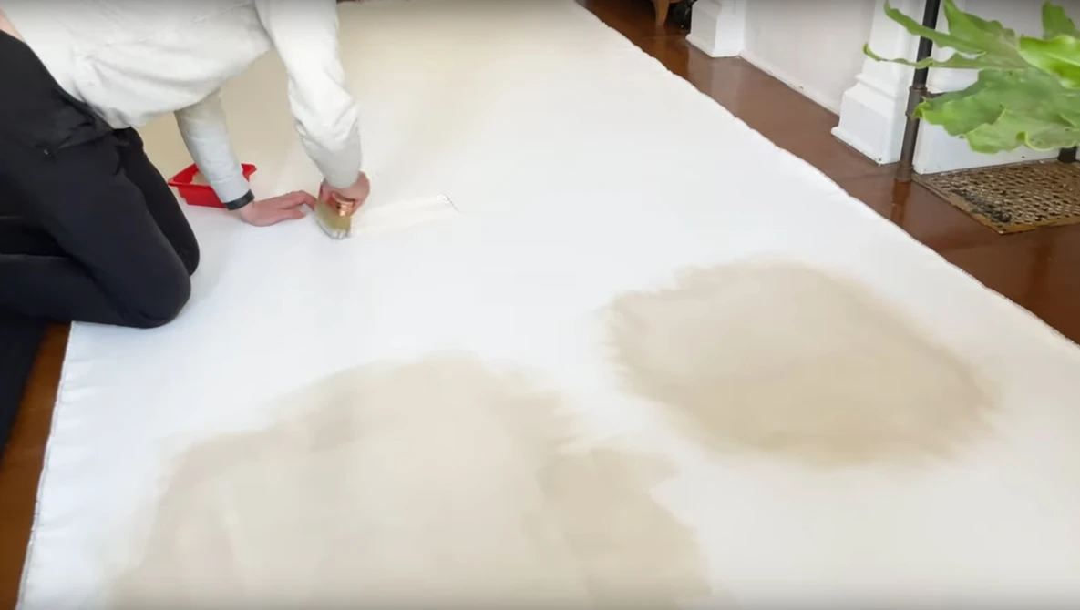 Person kneeling beside white paper with blurred footprints or impressions visible on the surface.