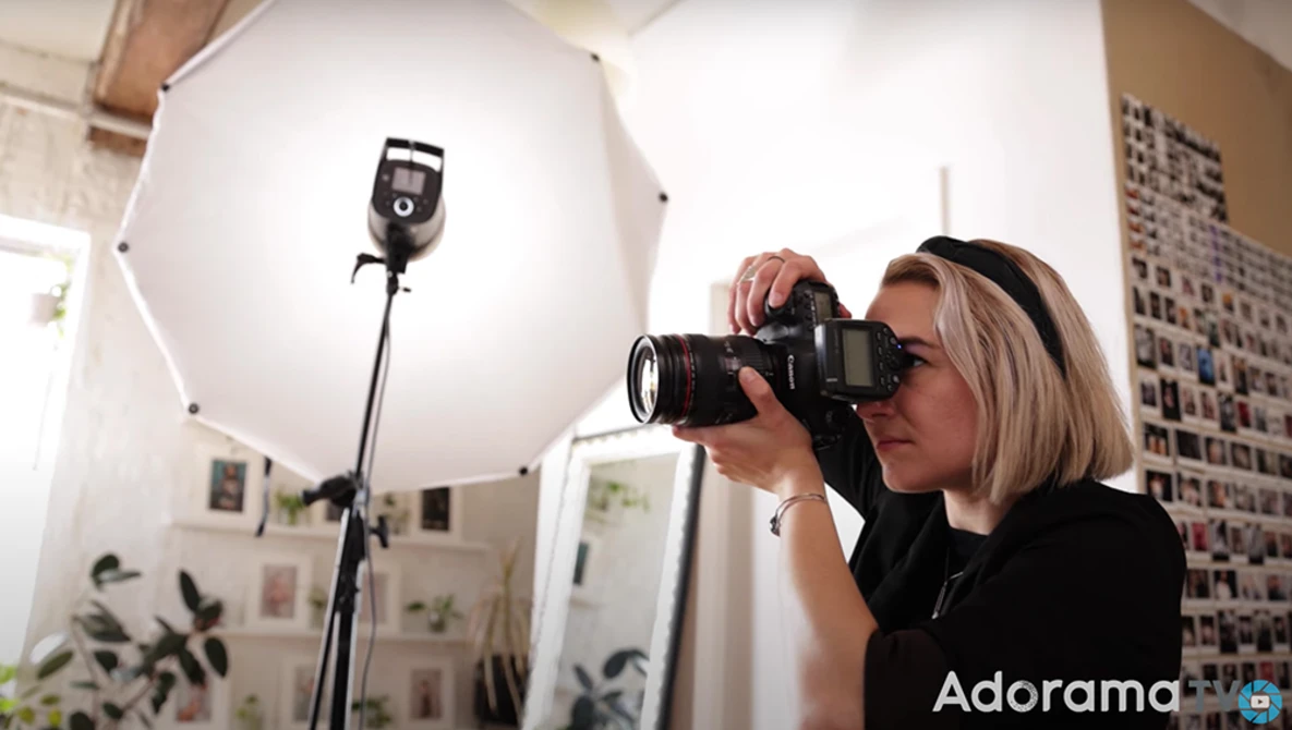 Photographer holding a camera with telephoto lens in a studio with large softbox lighting setup.