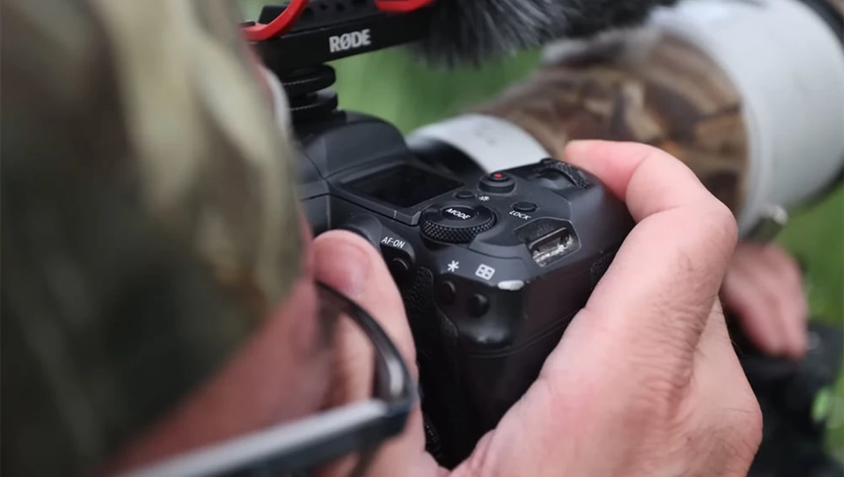 Filmmaker's hand holding a compact wireless audio receiver with buttons and a USB port visible.